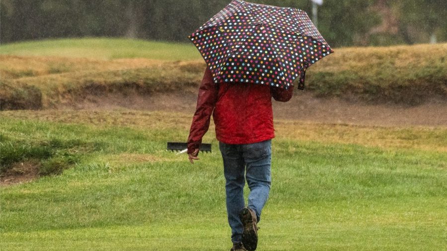 Una persona camina con paraguas por la cancha bajo la lluvia